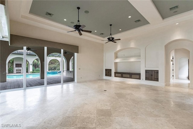 unfurnished living room featuring ceiling fan, a raised ceiling, and a high ceiling