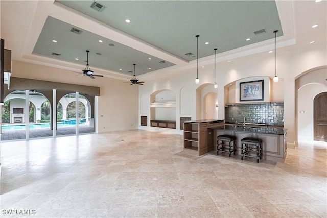 kitchen with a breakfast bar, a tray ceiling, ceiling fan, a spacious island, and hanging light fixtures