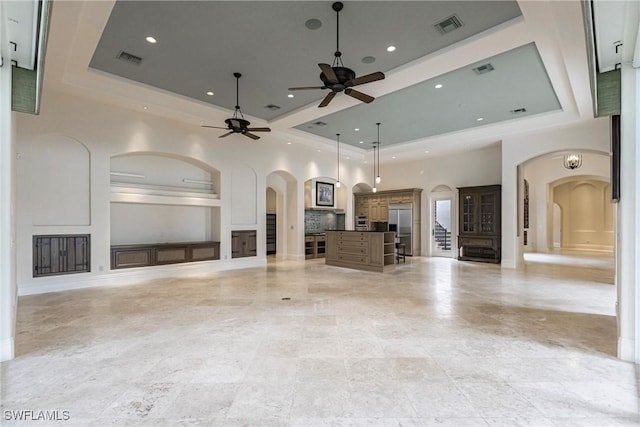 unfurnished living room with ceiling fan, a raised ceiling, and a towering ceiling