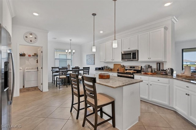 kitchen featuring a breakfast bar, stainless steel appliances, washer and clothes dryer, decorative light fixtures, and white cabinets