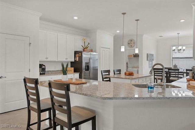 kitchen with stainless steel refrigerator with ice dispenser, sink, white cabinetry, hanging light fixtures, and an island with sink