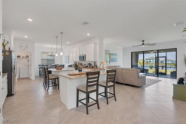 kitchen with appliances with stainless steel finishes, a breakfast bar, ceiling fan with notable chandelier, white cabinets, and hanging light fixtures