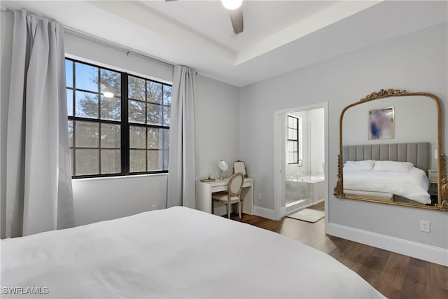 bedroom featuring ceiling fan, ensuite bath, a tray ceiling, and dark hardwood / wood-style flooring