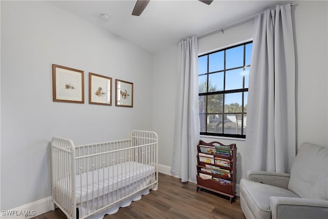 bedroom featuring dark hardwood / wood-style flooring, a nursery area, and ceiling fan