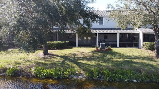 rear view of property featuring a water view, a yard, and a sunroom