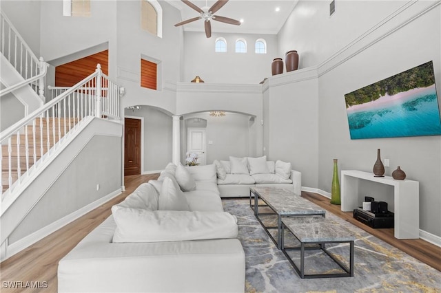 living room with decorative columns, ceiling fan, a towering ceiling, and wood-type flooring