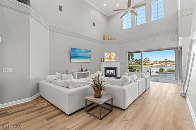 living room with a towering ceiling, ornamental molding, ceiling fan, light hardwood / wood-style flooring, and a multi sided fireplace