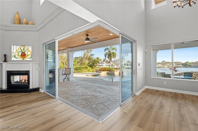 doorway featuring a multi sided fireplace, light hardwood / wood-style flooring, a water view, and ceiling fan with notable chandelier