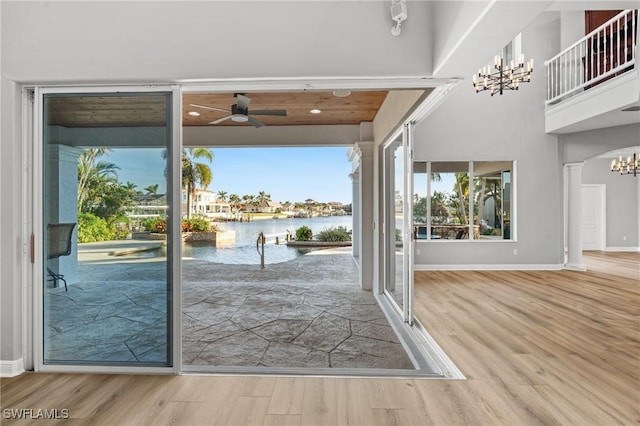 doorway with a water view, a healthy amount of sunlight, ceiling fan with notable chandelier, and hardwood / wood-style flooring