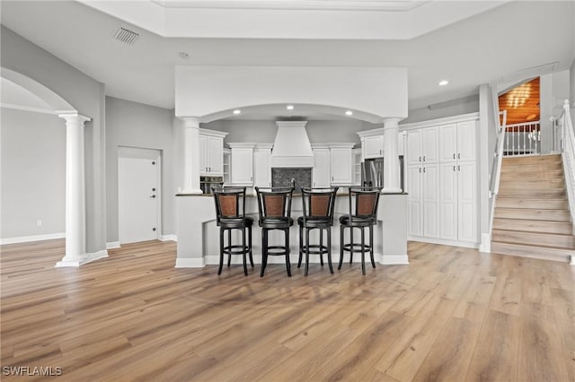 kitchen featuring a kitchen bar, tasteful backsplash, white cabinets, stainless steel fridge with ice dispenser, and light hardwood / wood-style floors