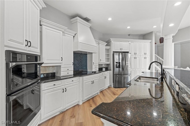 kitchen with tasteful backsplash, white cabinets, stainless steel fridge, double wall oven, and custom range hood