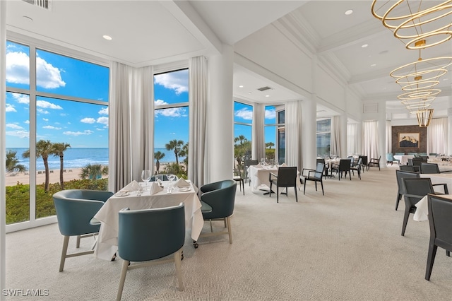 carpeted dining area with beam ceiling, coffered ceiling, expansive windows, a chandelier, and a water view