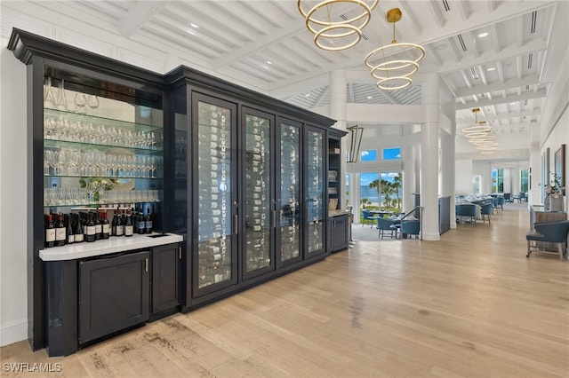 bar featuring pendant lighting, plenty of natural light, light hardwood / wood-style floors, and an inviting chandelier