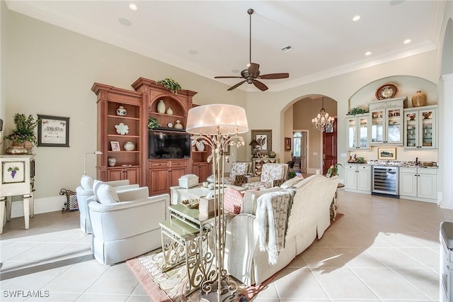 living room with ceiling fan with notable chandelier, light tile patterned floors, crown molding, and beverage cooler