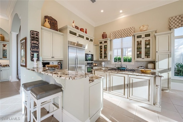 kitchen with built in appliances, light stone counters, light tile patterned floors, and ornate columns