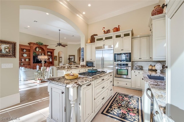 kitchen featuring a center island, built in appliances, ceiling fan, light tile patterned flooring, and light stone counters