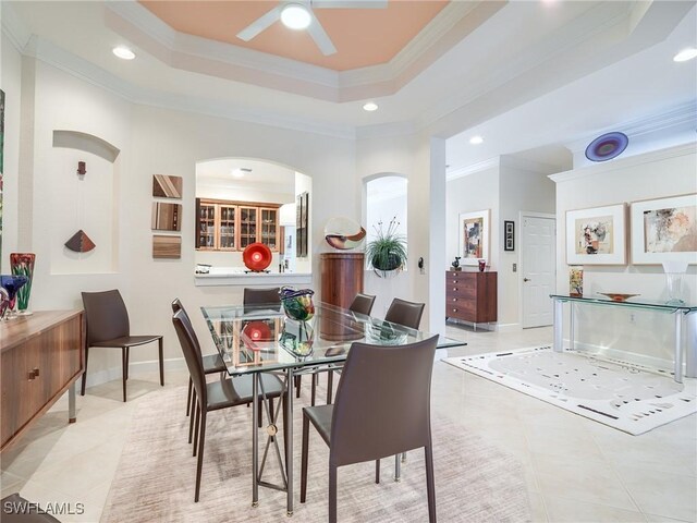 tiled dining room featuring a raised ceiling, ceiling fan, and ornamental molding