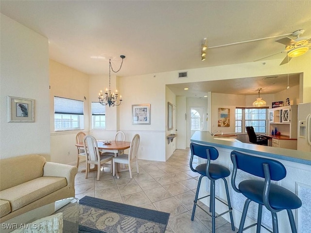 kitchen with a kitchen bar, ceiling fan with notable chandelier, a healthy amount of sunlight, decorative light fixtures, and light tile patterned flooring