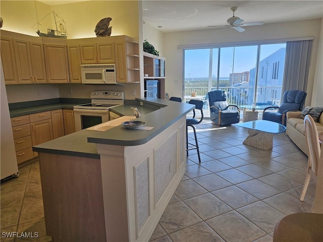 kitchen with a kitchen breakfast bar, white appliances, ceiling fan, and light brown cabinetry