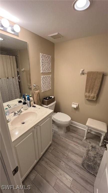 bathroom with hardwood / wood-style floors, vanity, toilet, and walk in shower