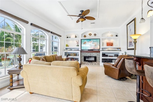 tiled living room featuring built in shelves, ceiling fan, a fireplace, and ornamental molding