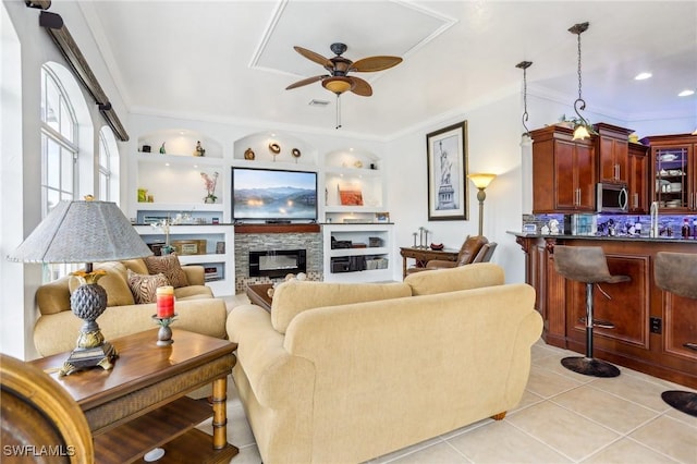 living room with light tile patterned floors, ceiling fan, ornamental molding, a fireplace, and built in features