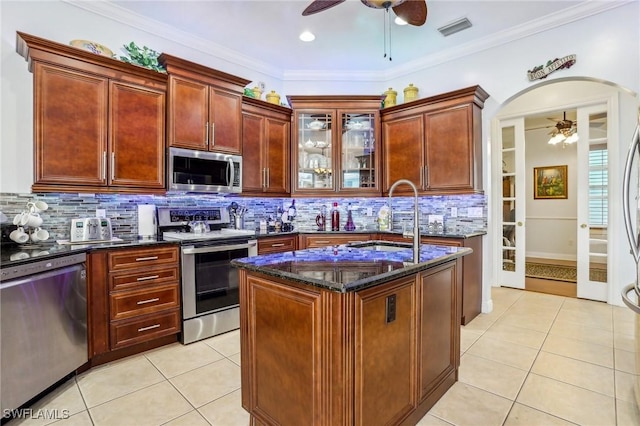 kitchen with sink, dark stone countertops, light tile patterned floors, a kitchen island, and appliances with stainless steel finishes