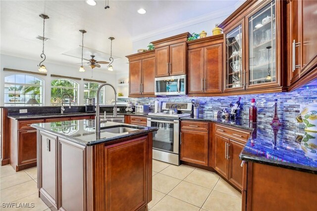 kitchen with stainless steel appliances, light tile patterned floors, dark stone counters, hanging light fixtures, and a kitchen island with sink