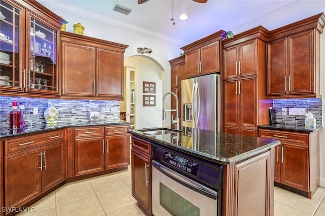 kitchen with stainless steel appliances, a center island with sink, tasteful backsplash, and dark stone counters