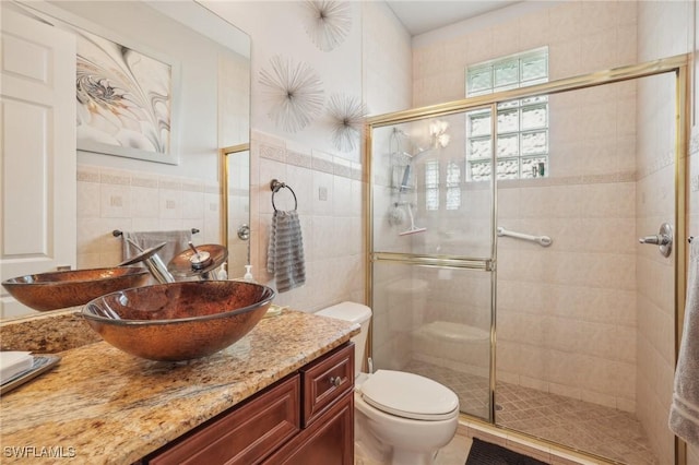 bathroom featuring toilet, a shower with door, vanity, and tile walls