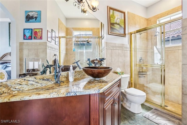 bathroom with toilet, vanity, tile walls, a notable chandelier, and a shower with shower door