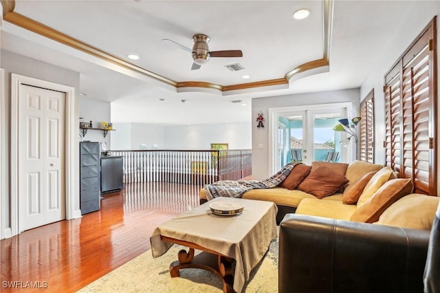 living room with french doors, hardwood / wood-style floors, a tray ceiling, crown molding, and ceiling fan