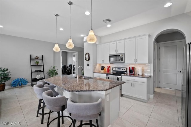 kitchen with dark stone counters, stainless steel appliances, sink, a center island with sink, and white cabinets