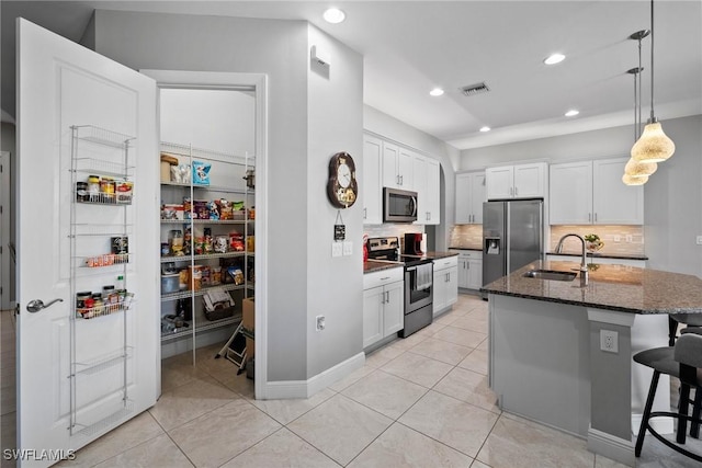 kitchen with appliances with stainless steel finishes, dark stone counters, a kitchen island with sink, sink, and white cabinetry