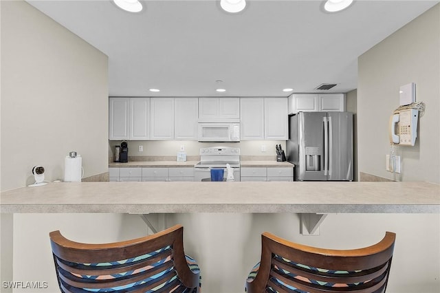 kitchen with a kitchen bar, kitchen peninsula, white cabinets, and white appliances