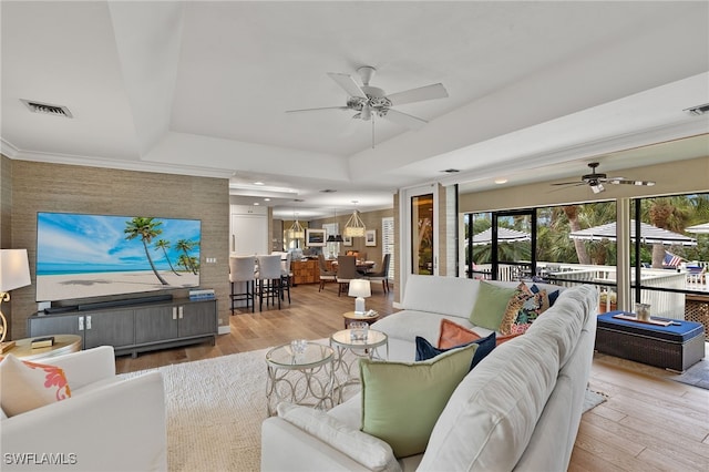 living room with a raised ceiling, ceiling fan, and light wood-type flooring