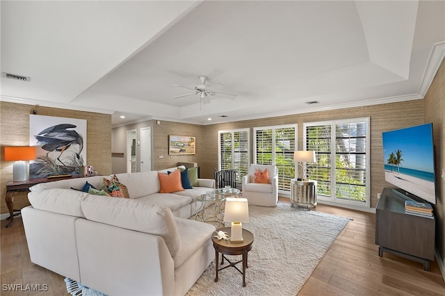 living room with ceiling fan, light hardwood / wood-style floors, a raised ceiling, and crown molding