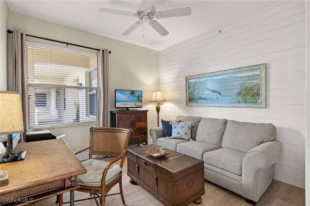 living area with a ceiling fan, light wood-type flooring, and wood walls