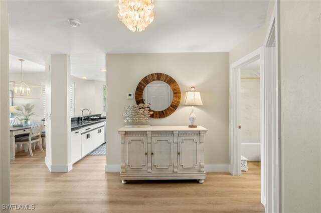 corridor with light wood-style floors, a sink, baseboards, and an inviting chandelier