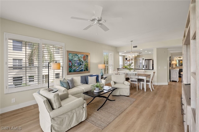 living room featuring ceiling fan with notable chandelier and light wood-type flooring