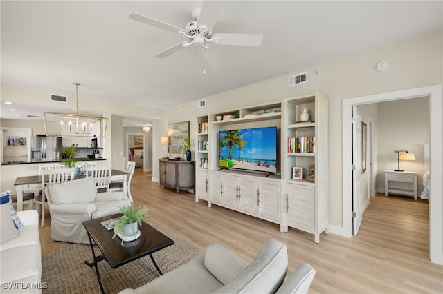 living area with visible vents, light wood-style flooring, and ceiling fan with notable chandelier