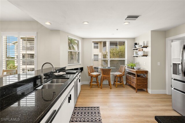 kitchen featuring visible vents, white cabinets, stainless steel appliances, light wood-type flooring, and a sink