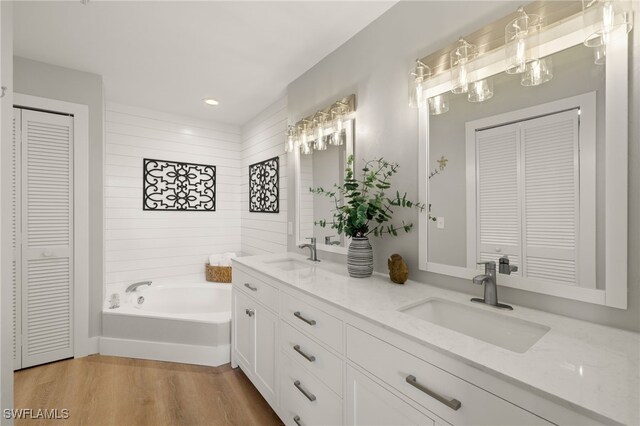 bathroom featuring a garden tub, wood finished floors, a closet, and a sink