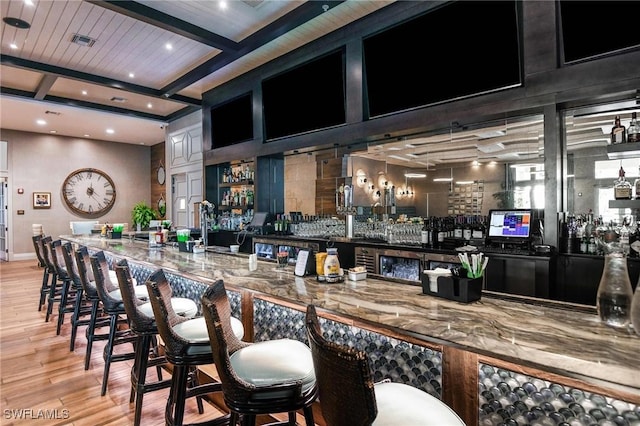 bar featuring stone counters, beamed ceiling, light hardwood / wood-style floors, and coffered ceiling