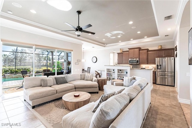 tiled living room with a raised ceiling, ceiling fan, and ornamental molding