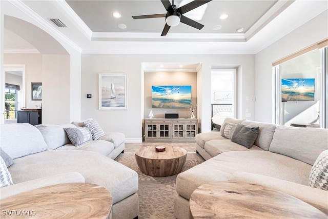 living room with a raised ceiling, crown molding, and ceiling fan