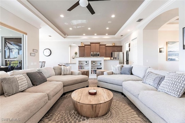 living room with a raised ceiling, ceiling fan, and crown molding