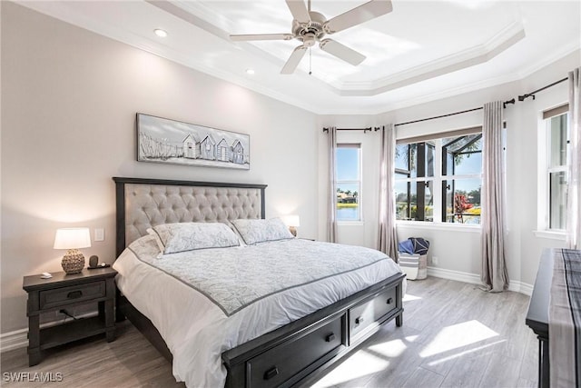 bedroom with light wood-type flooring, a tray ceiling, ceiling fan, and ornamental molding