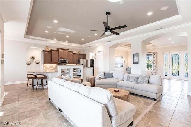 tiled living room featuring a tray ceiling, ceiling fan, crown molding, and stacked washer / drying machine