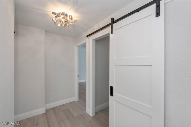 hallway featuring light wood-style floors, a barn door, and baseboards